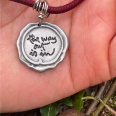 Plum Village pendant with ‘The Way Out Is In’ mantra against a tree